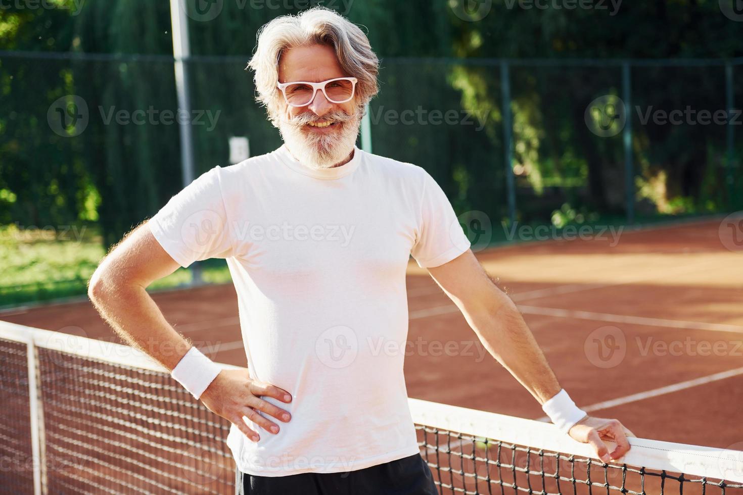 posando para una cámara. en gafas de sol. Senior hombre moderno y elegante al aire libre en el campo deportivo durante el día foto