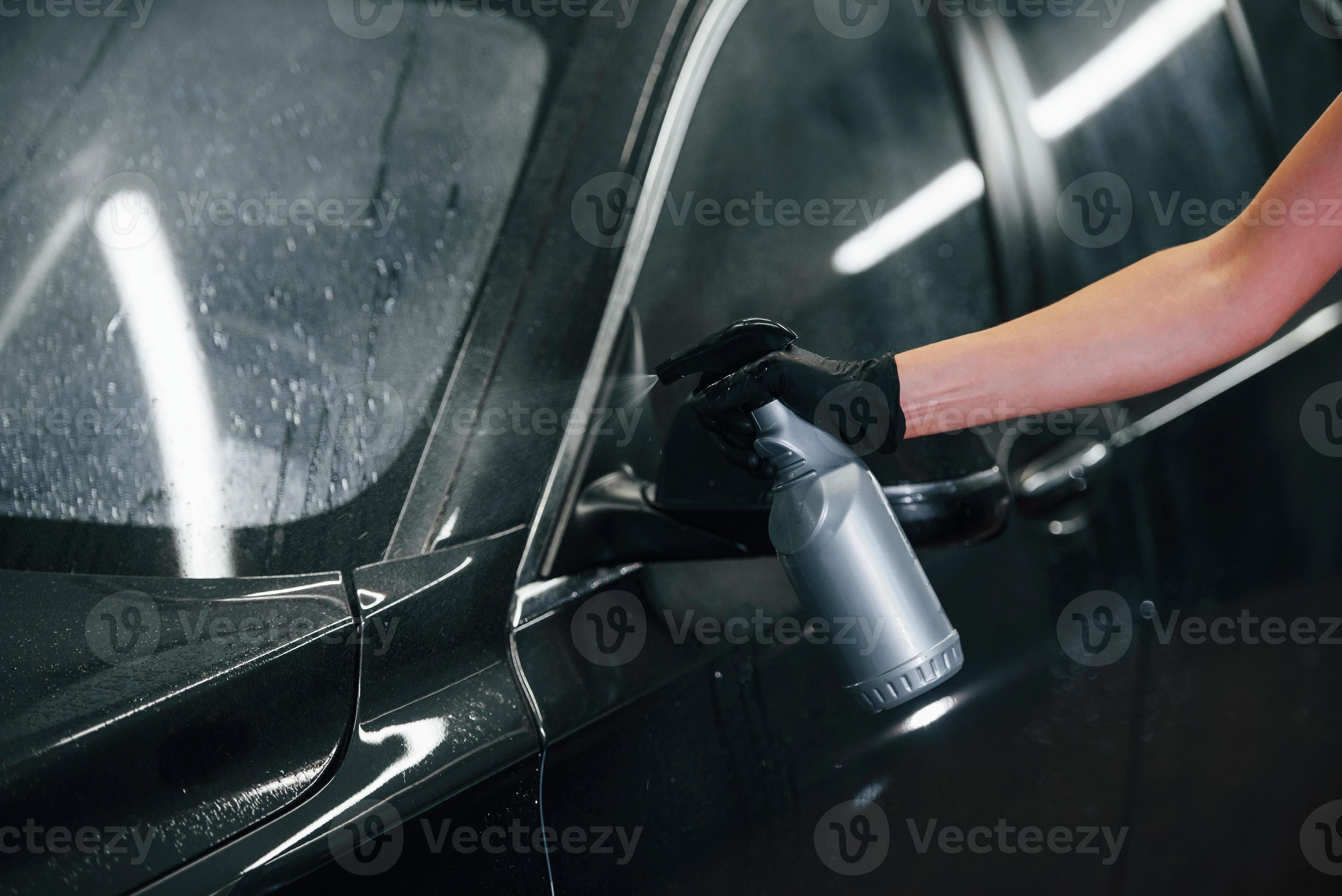 Spraying the vehicle. Modern black automobile get cleaned by woman