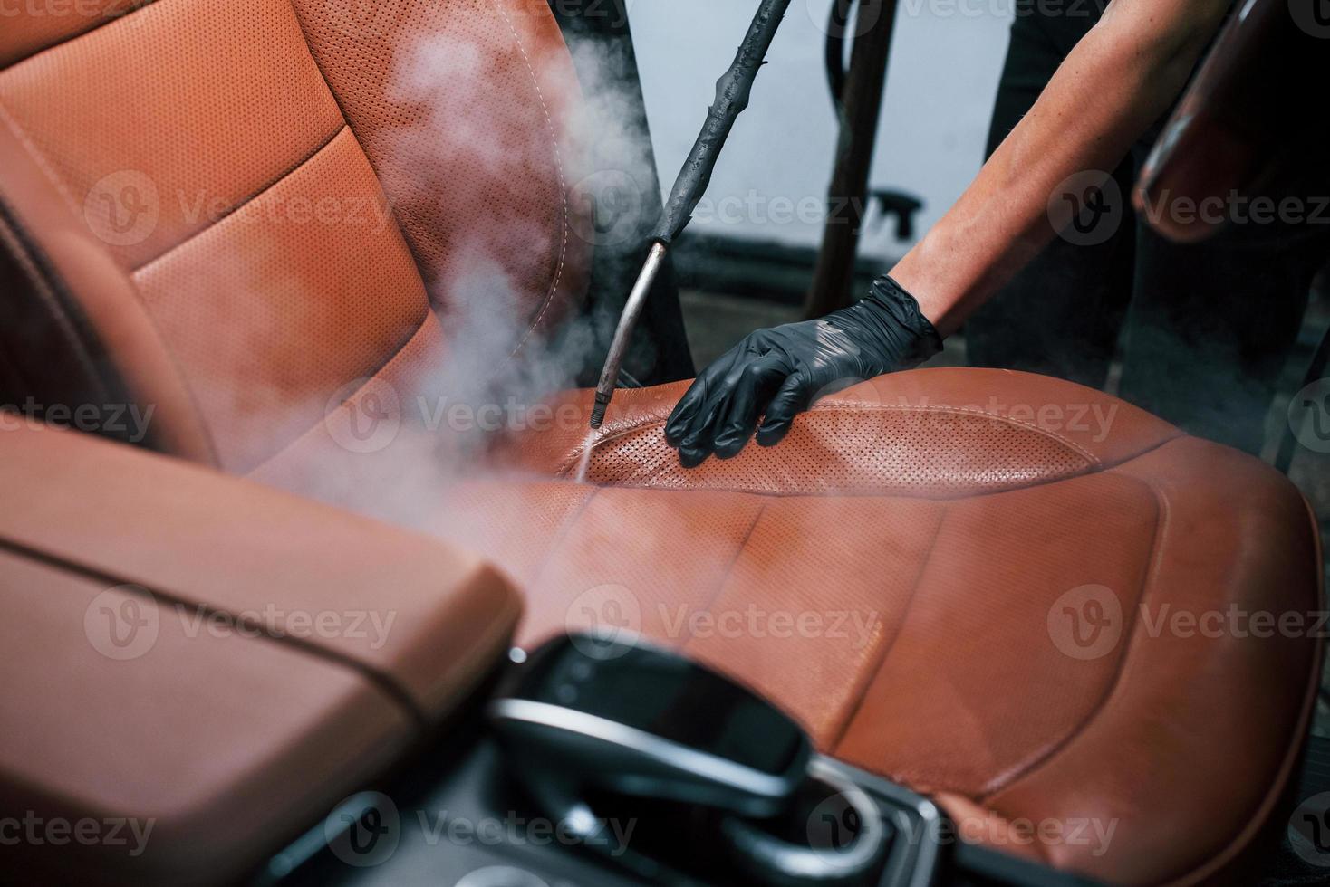 Uses steam cleaner. Modern black automobile is in service by woman inside of car wash station photo