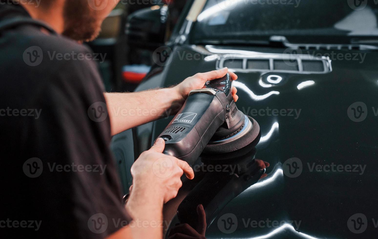 Guy polishing surface of vehicle. Modern black automobile get cleaned by man inside of car wash station photo