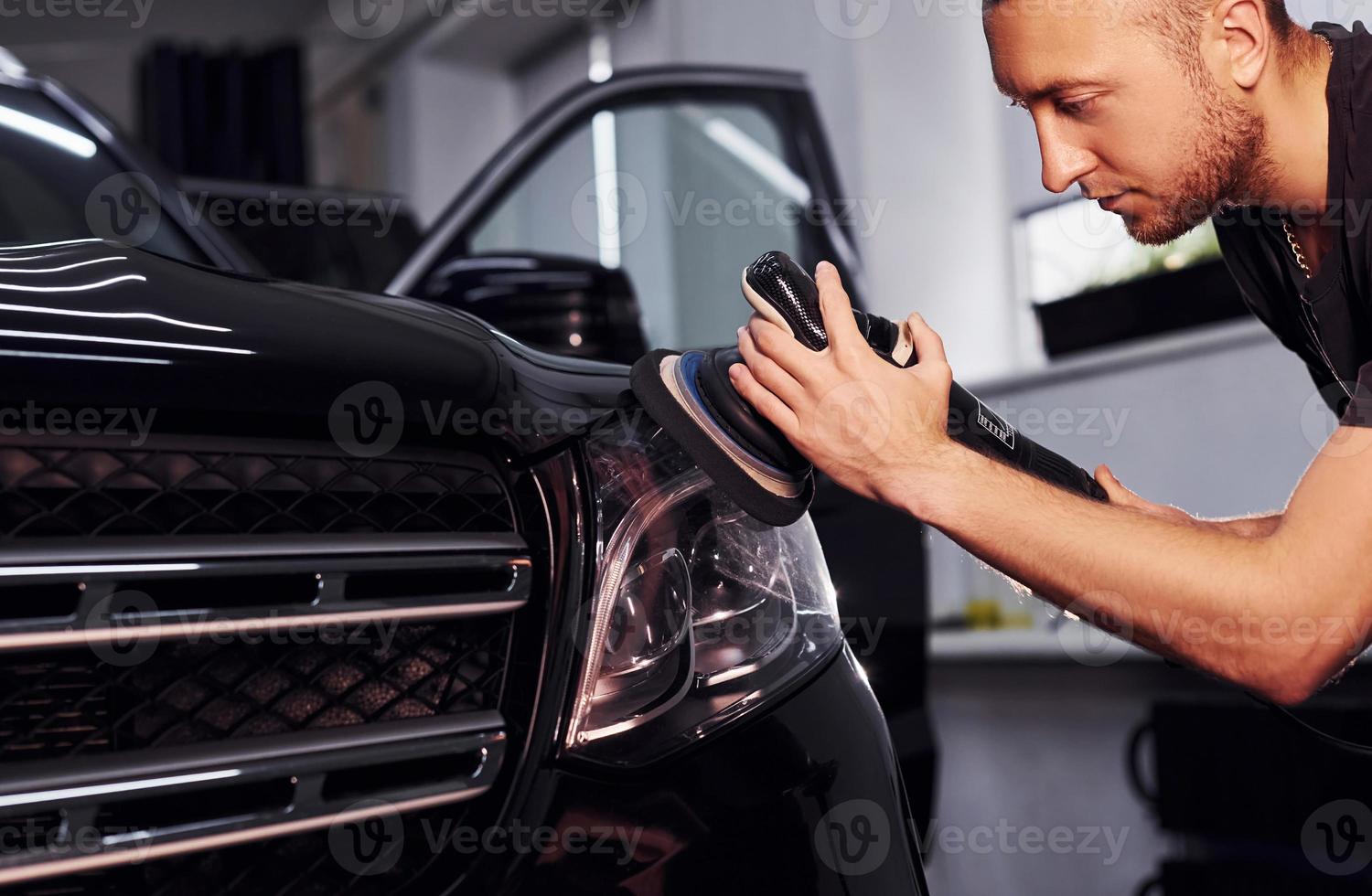 Guy polishing surface of vehicle. Modern black automobile get cleaned by man inside of car wash station photo