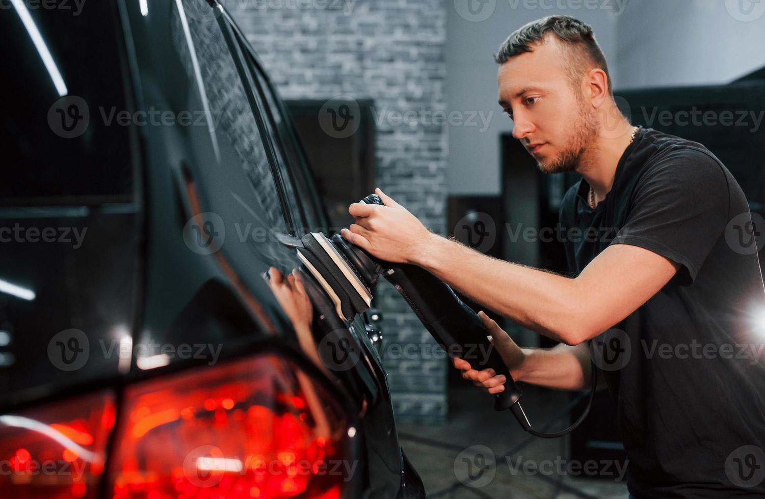 guy puliendo la superficie del vehículo. el automóvil negro moderno es limpiado por el hombre dentro de la estación de lavado de autos foto