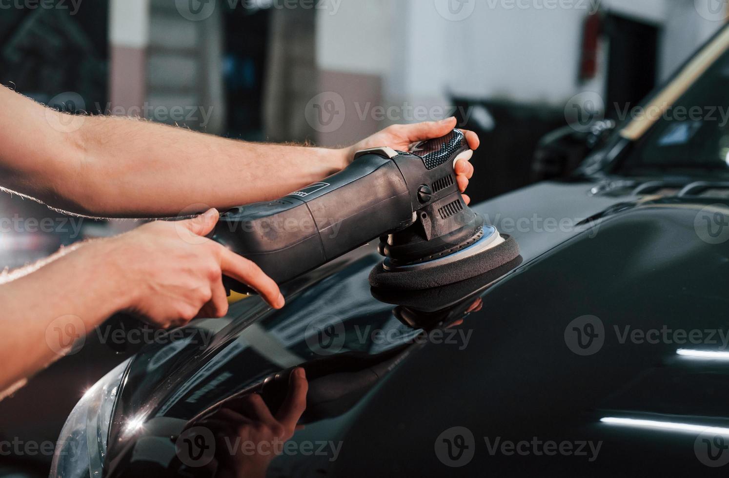Guy polishing surface of vehicle. Modern black automobile get cleaned by man inside of car wash station photo
