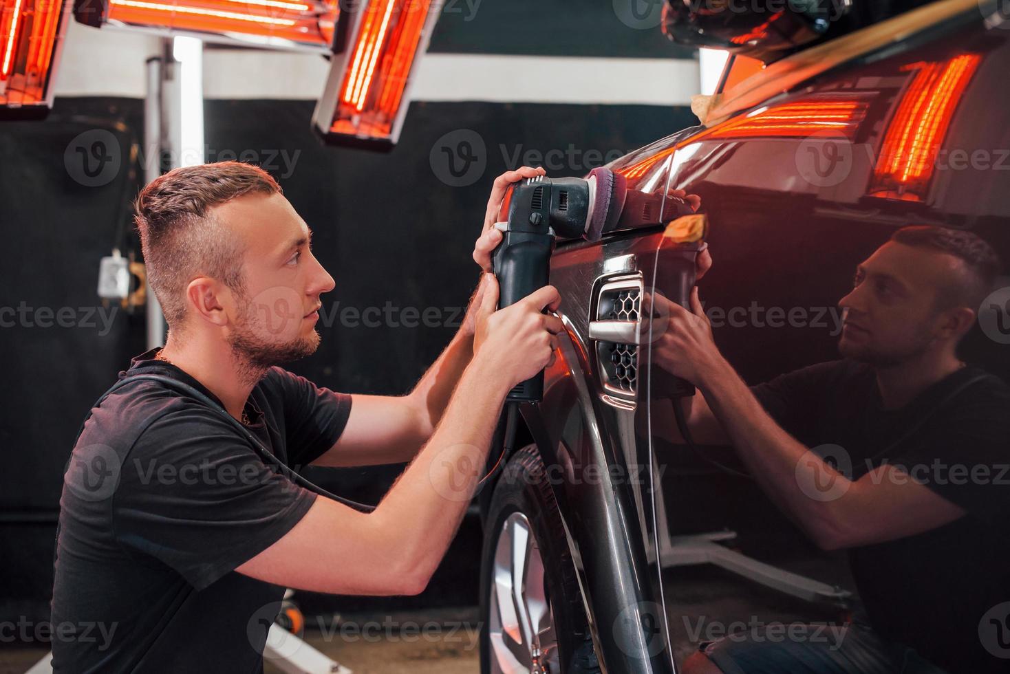 Guy polishing surface of vehicle. Modern black automobile get cleaned by man inside of car wash station photo