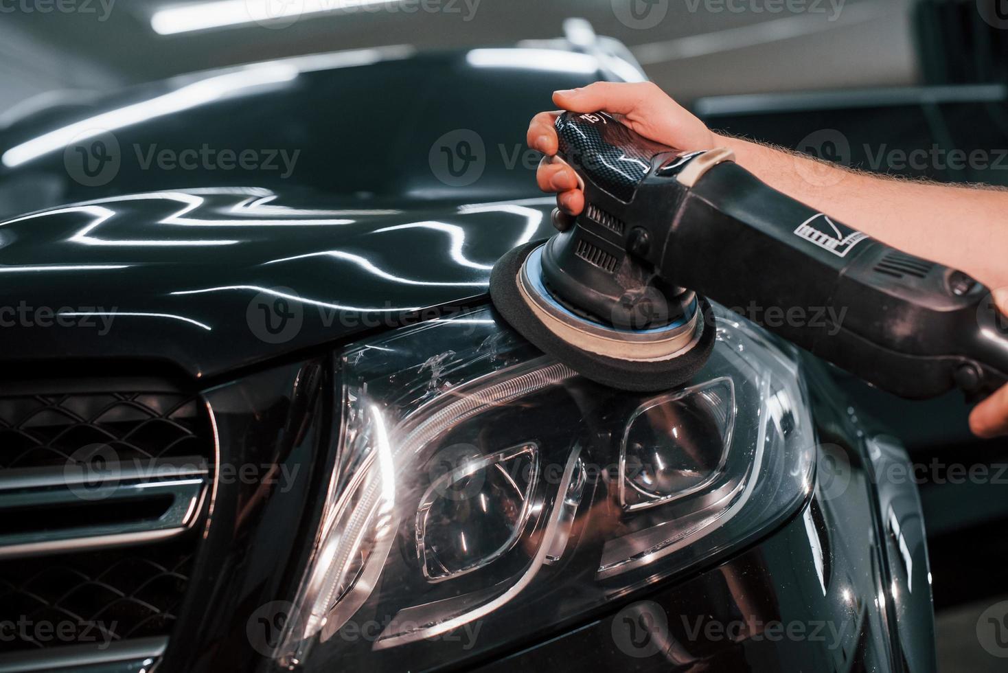 Guy polishing surface of vehicle. Modern black automobile get cleaned by man inside of car wash station photo