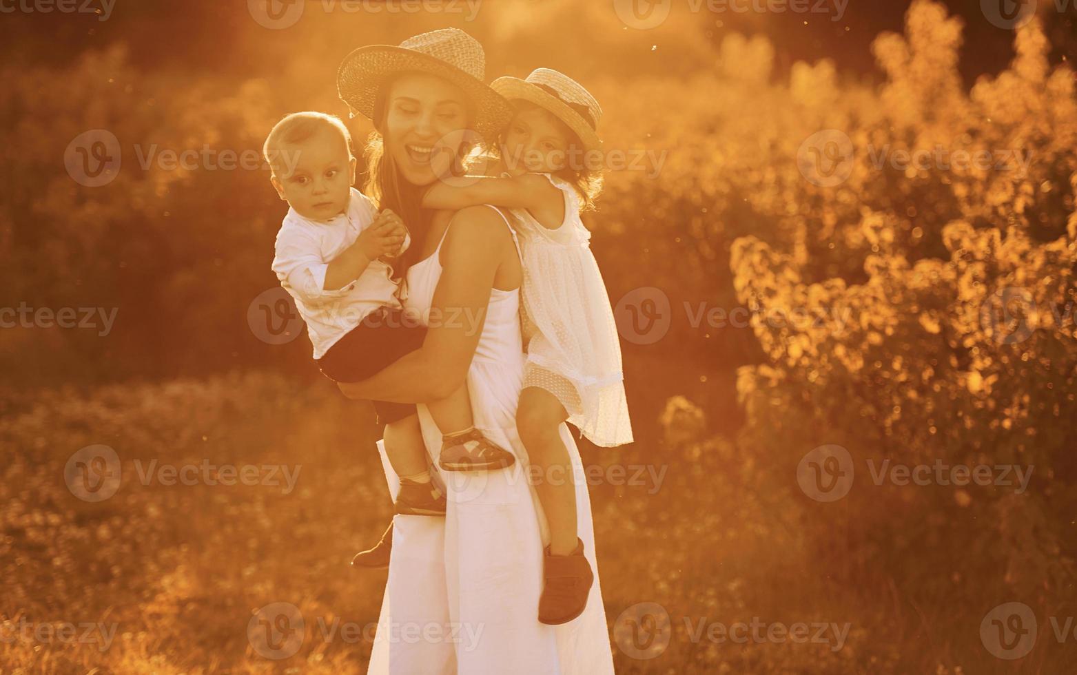Happy family of mother, little son and daughter spending free time on the field at sunny day time of summer photo