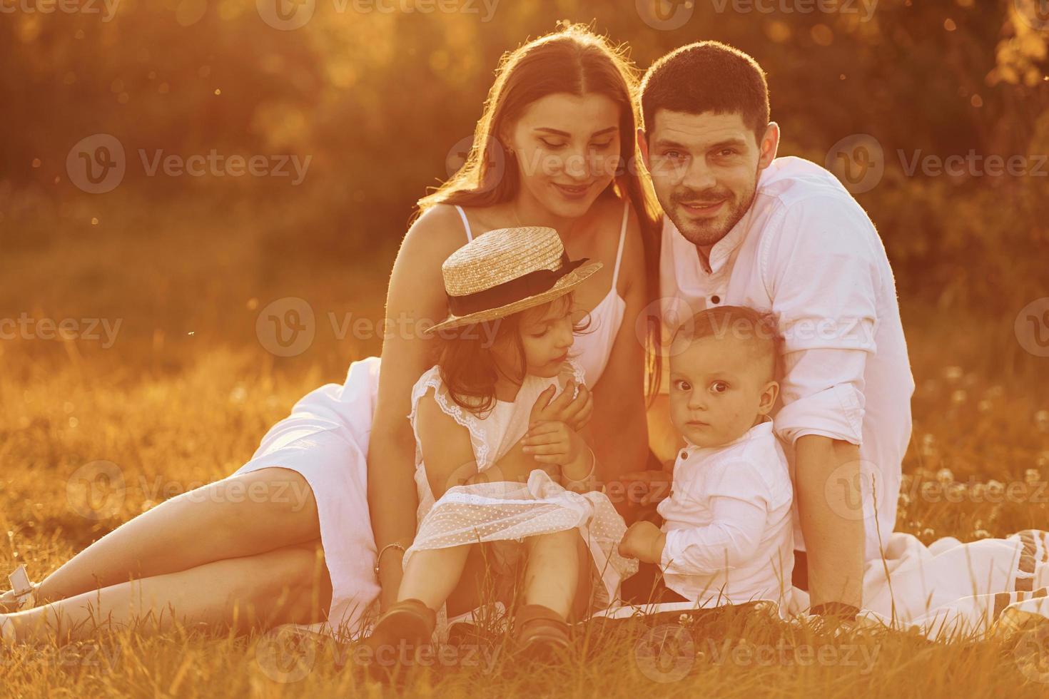 sentado en la hierba. padre, madre con hija e hijo pasando tiempo libre al aire libre en un día soleado de verano foto