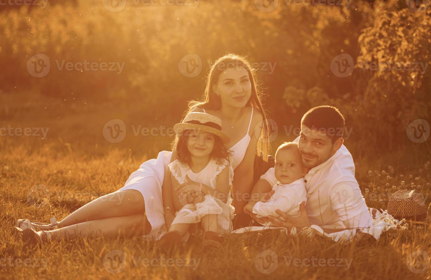 sentado en la hierba. padre, madre con hija e hijo pasando tiempo libre al aire libre en un día soleado de verano foto