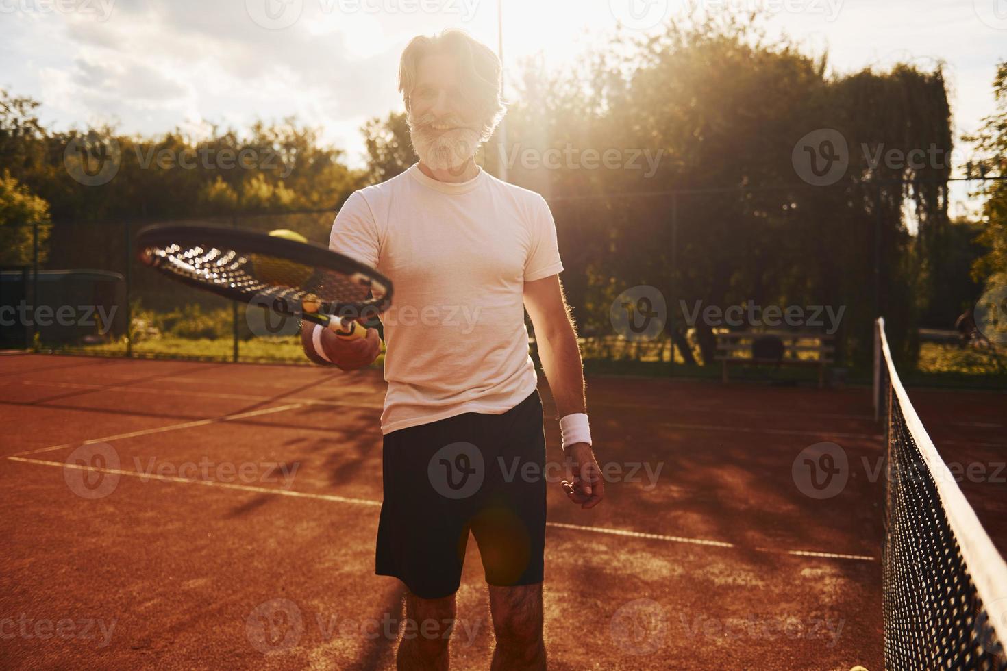 Training time. Senior modern stylish man with racket outdoors on tennis court at daytime photo