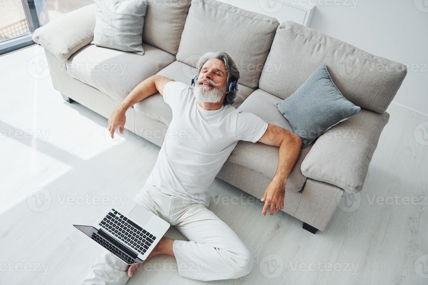 disfruta de la música. Senior hombre moderno con estilo con pelo gris y barba en el interior foto