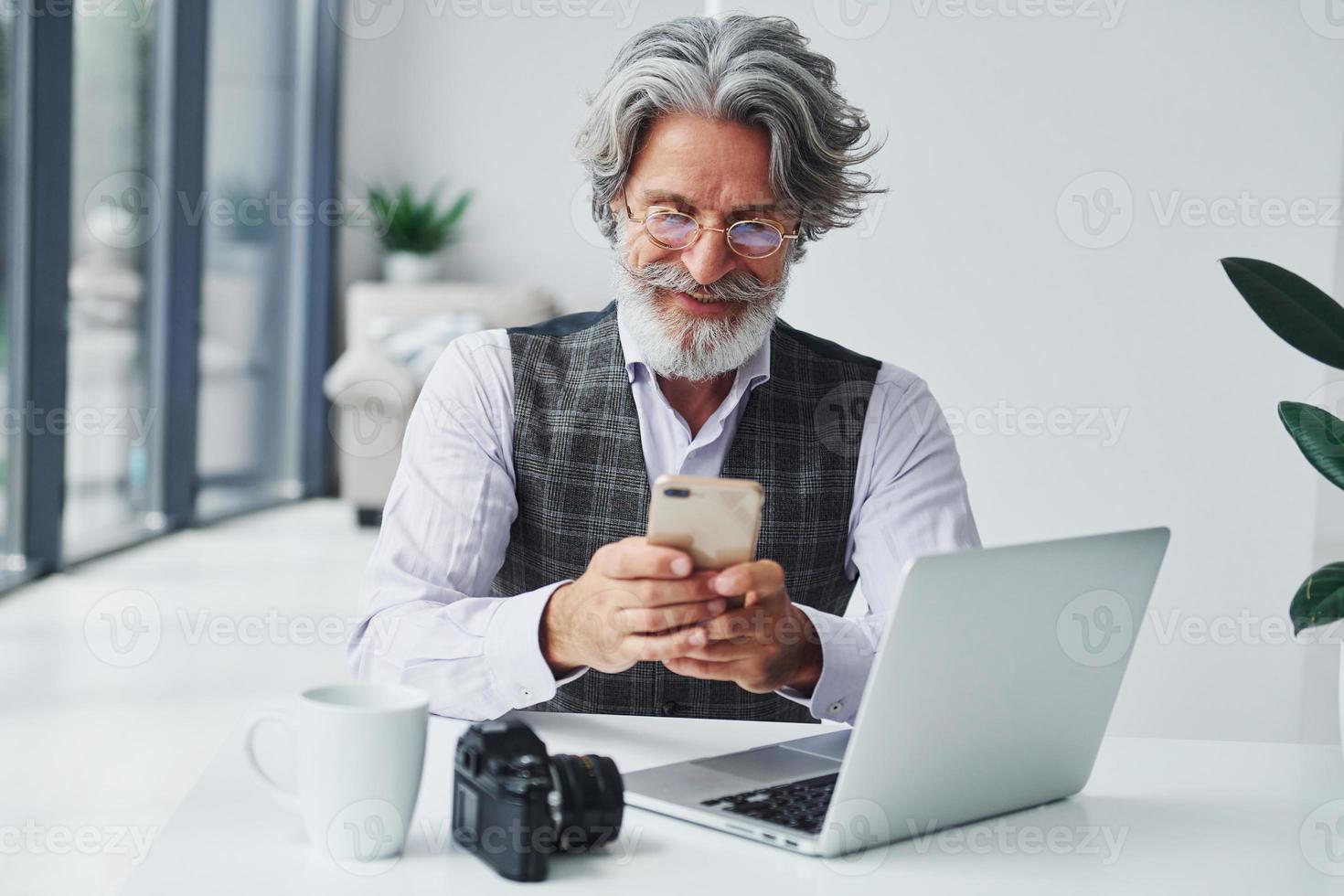 Boss in formal clothes works in office. Senior stylish modern man with grey hair and beard indoors photo