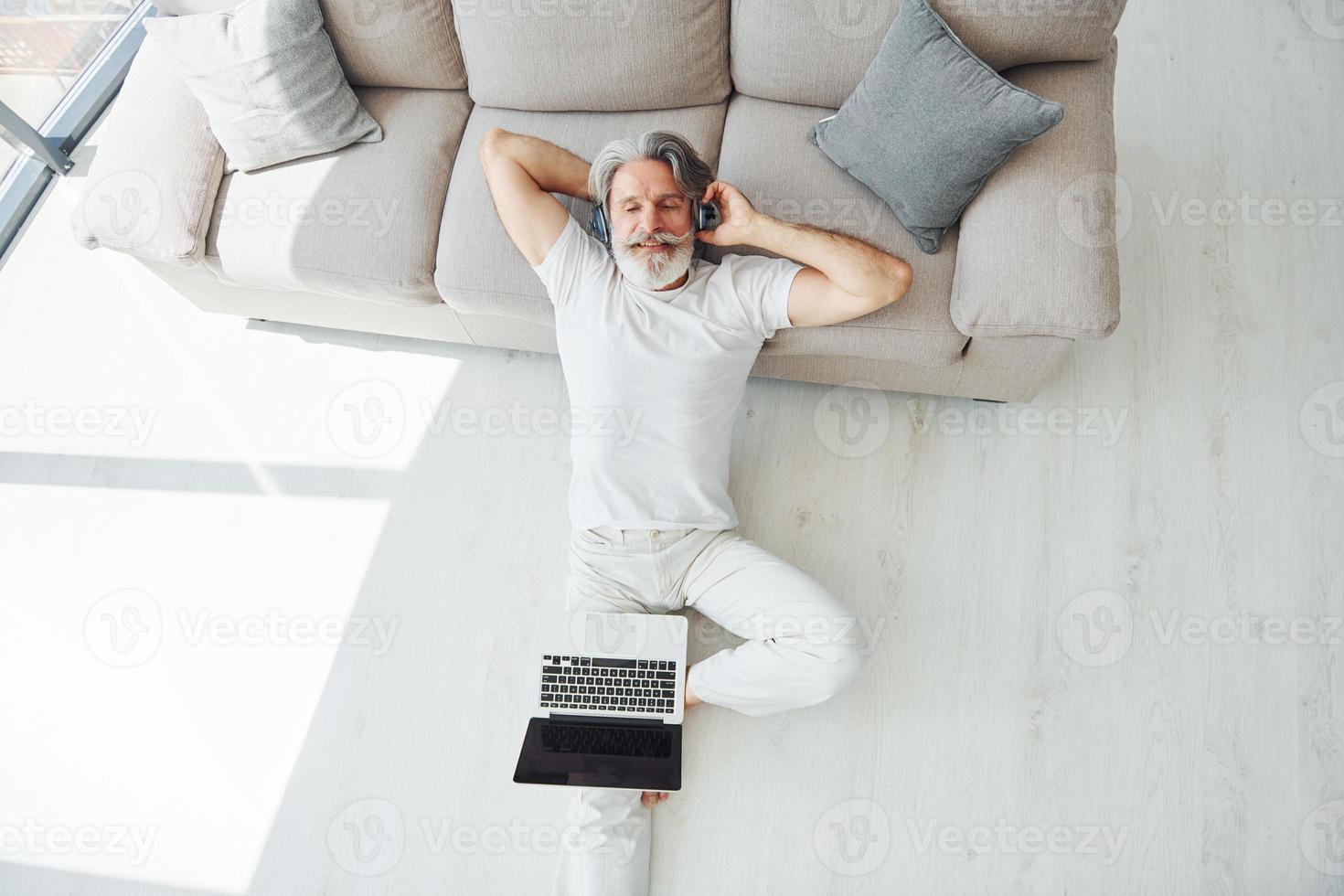 Enjoys music. Senior stylish modern man with grey hair and beard indoors photo