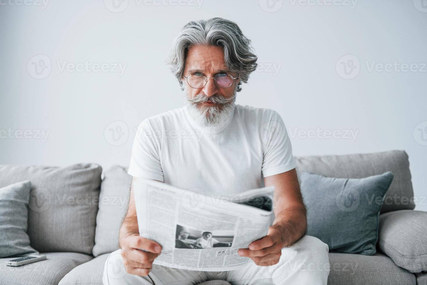 Sits on the sofa. Senior stylish modern man with grey hair and beard indoors photo