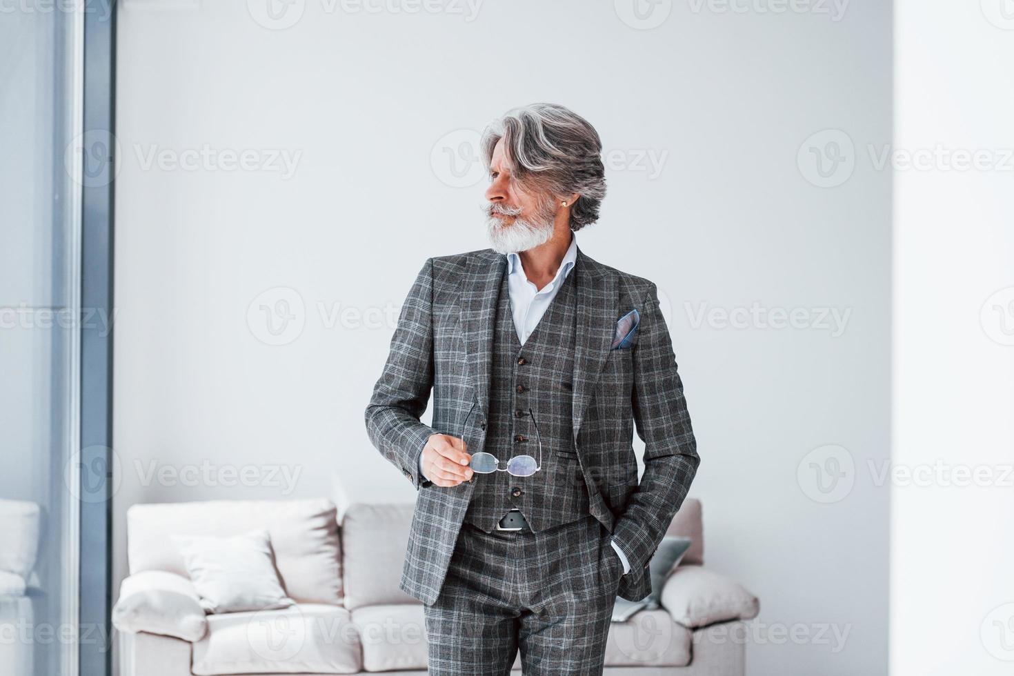In apartment with elegant clothes. Senior stylish modern man with grey hair and beard indoors photo