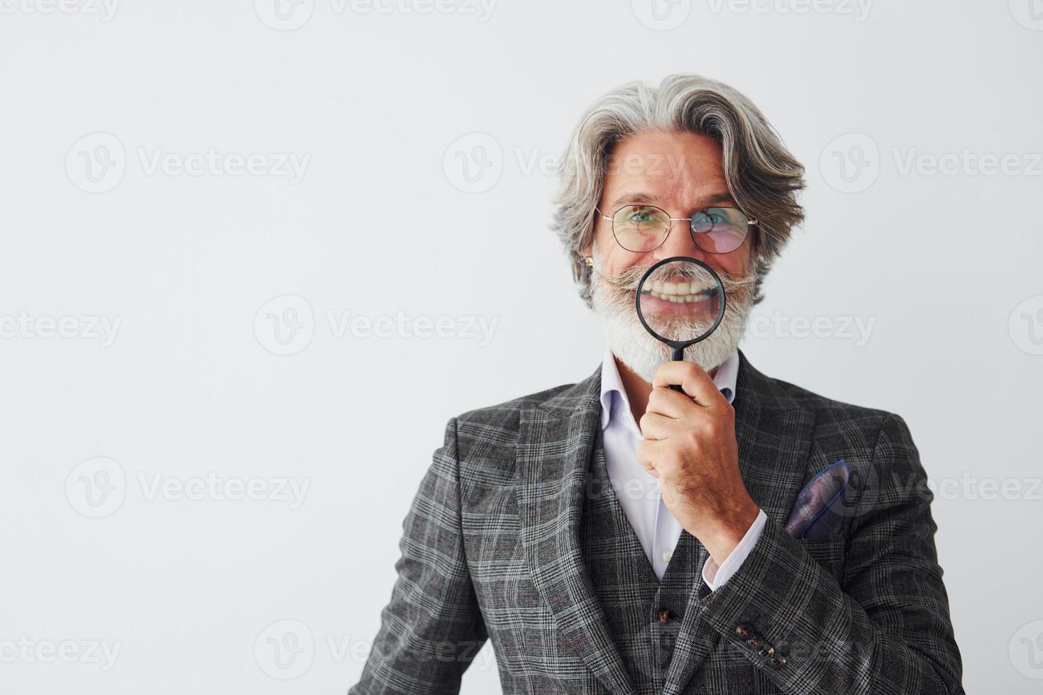 Having fun with magnifying glass. Senior stylish modern man with grey hair and beard indoors photo