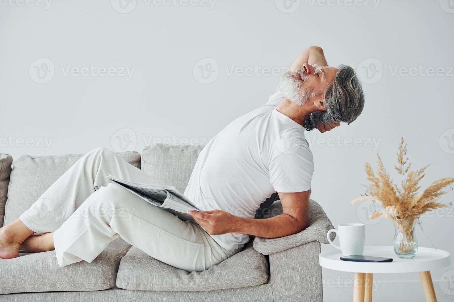 Sits on the sofa. Senior stylish modern man with grey hair and beard indoors photo