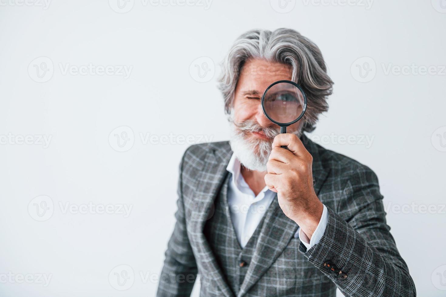 Having fun with magnifying glass. Senior stylish modern man with grey hair and beard indoors photo