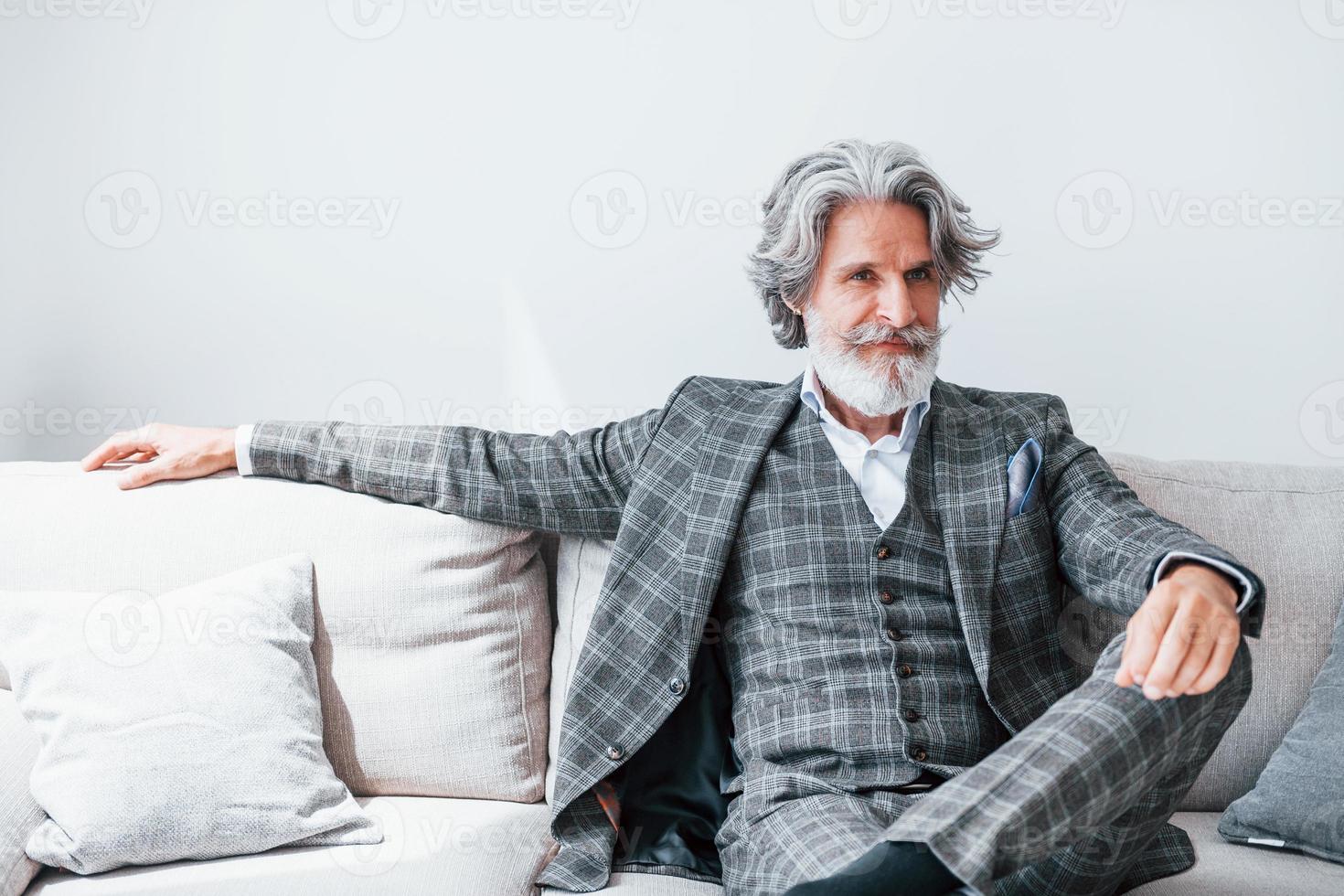 en apartamento con ropa elegante. Senior hombre moderno con estilo con pelo gris y barba en el interior foto