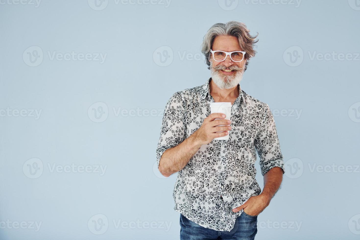 taza de bebida en las manos. Senior hombre moderno con estilo con pelo gris y barba en el interior foto