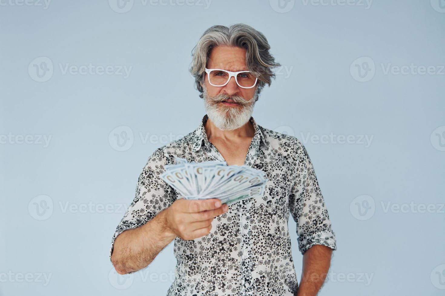 Millionaire with cash in hands. Senior stylish modern man with grey hair and beard indoors photo