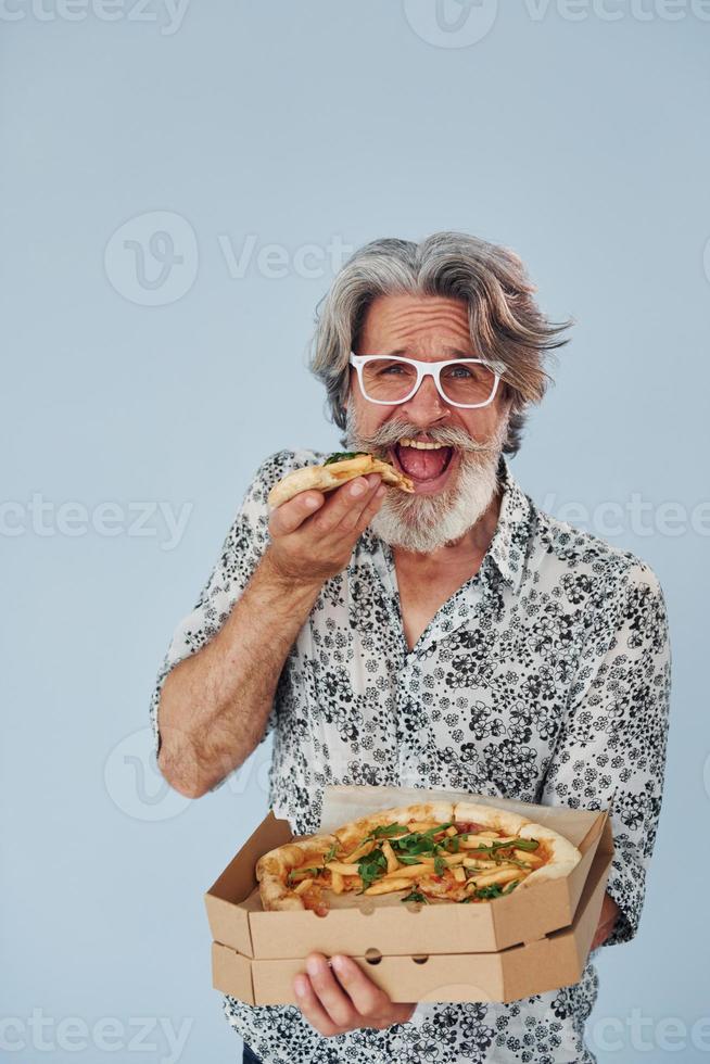 come pizza cuando está parado contra la pared. Senior hombre moderno con estilo con pelo gris y barba en el interior foto