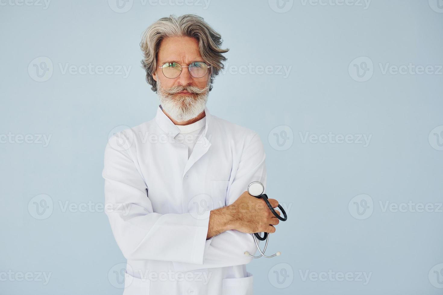 Doctor in white coat against wall. Senior stylish modern man with grey hair and beard indoors photo