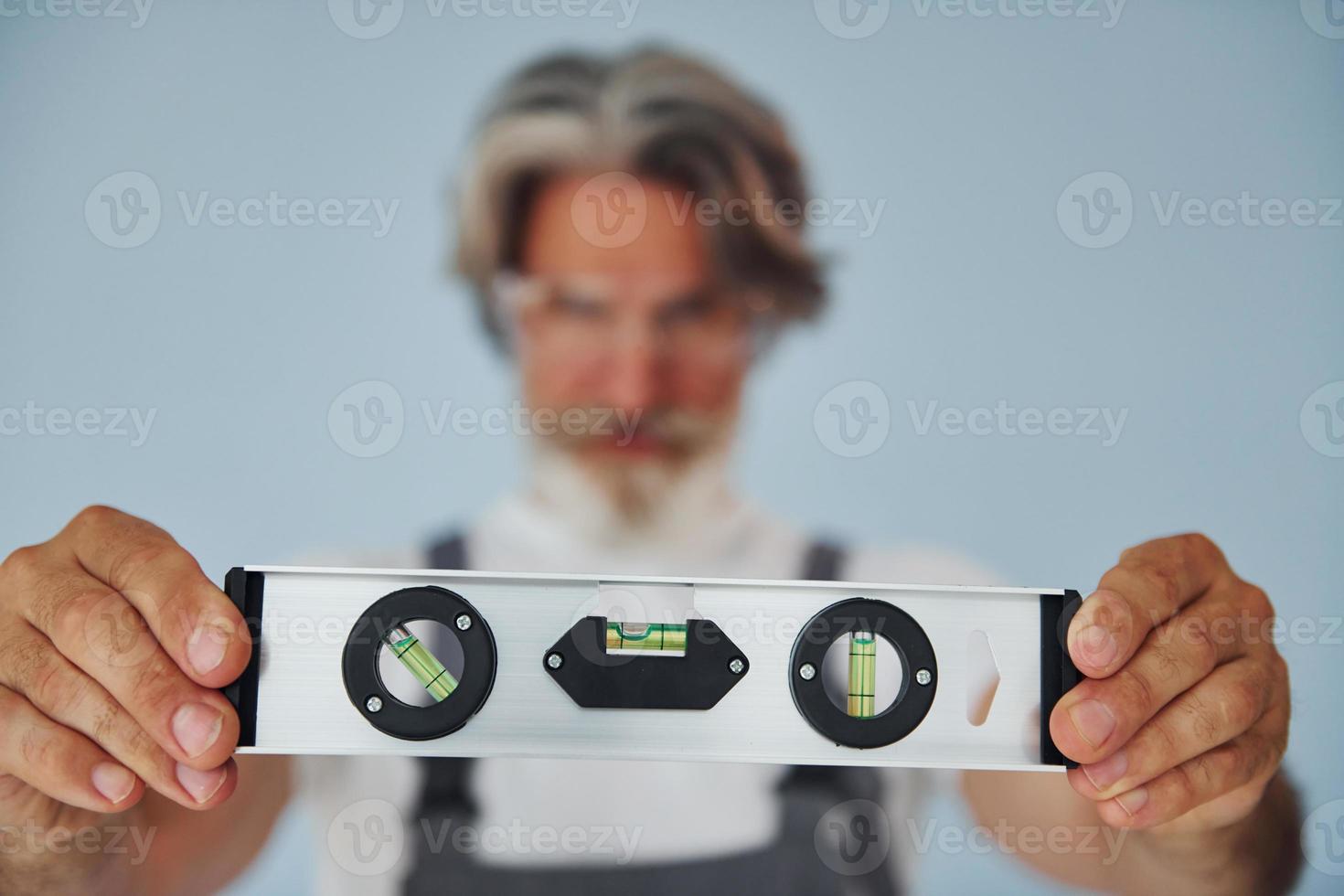 Worker in uniform holds level matching device. Senior stylish modern man with grey hair and beard indoors photo