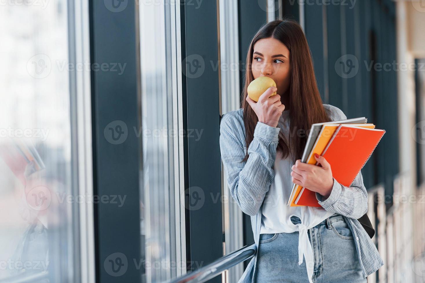 una joven estudiante está en el pasillo de una universidad, sosteniendo blocs de notas y una manzana foto