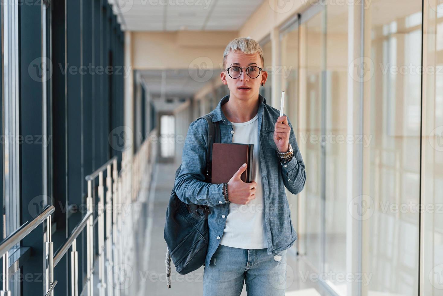 un joven estudiante con ropa de jeans está en el pasillo de una universidad con libros en las manos foto