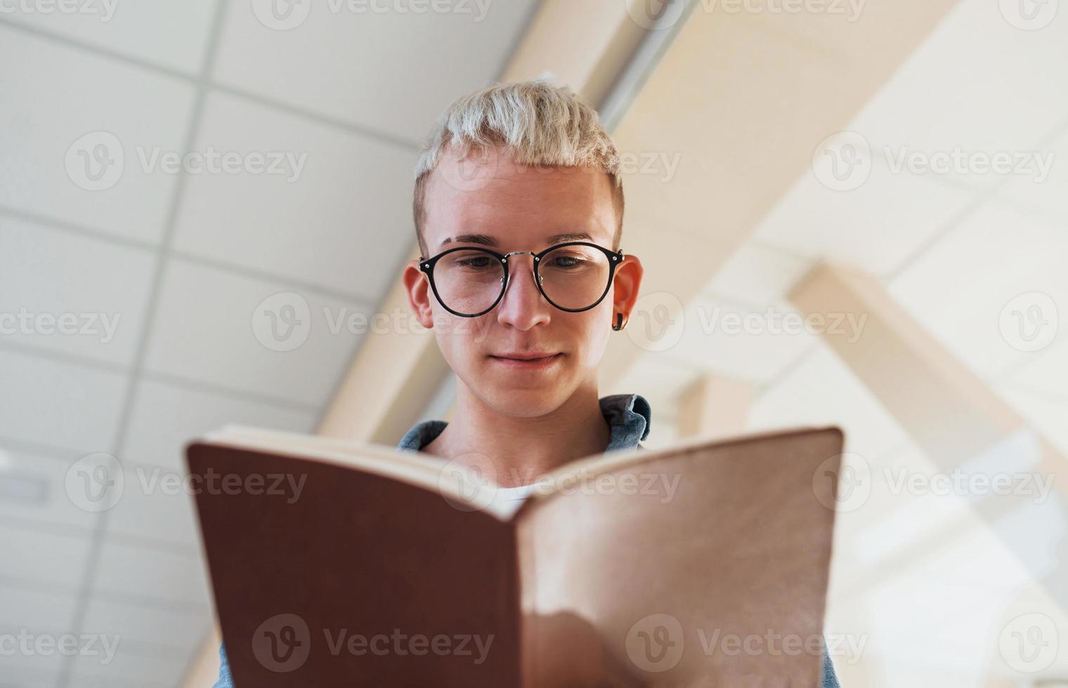 Young male college student in glasses reading book indoors 15299017