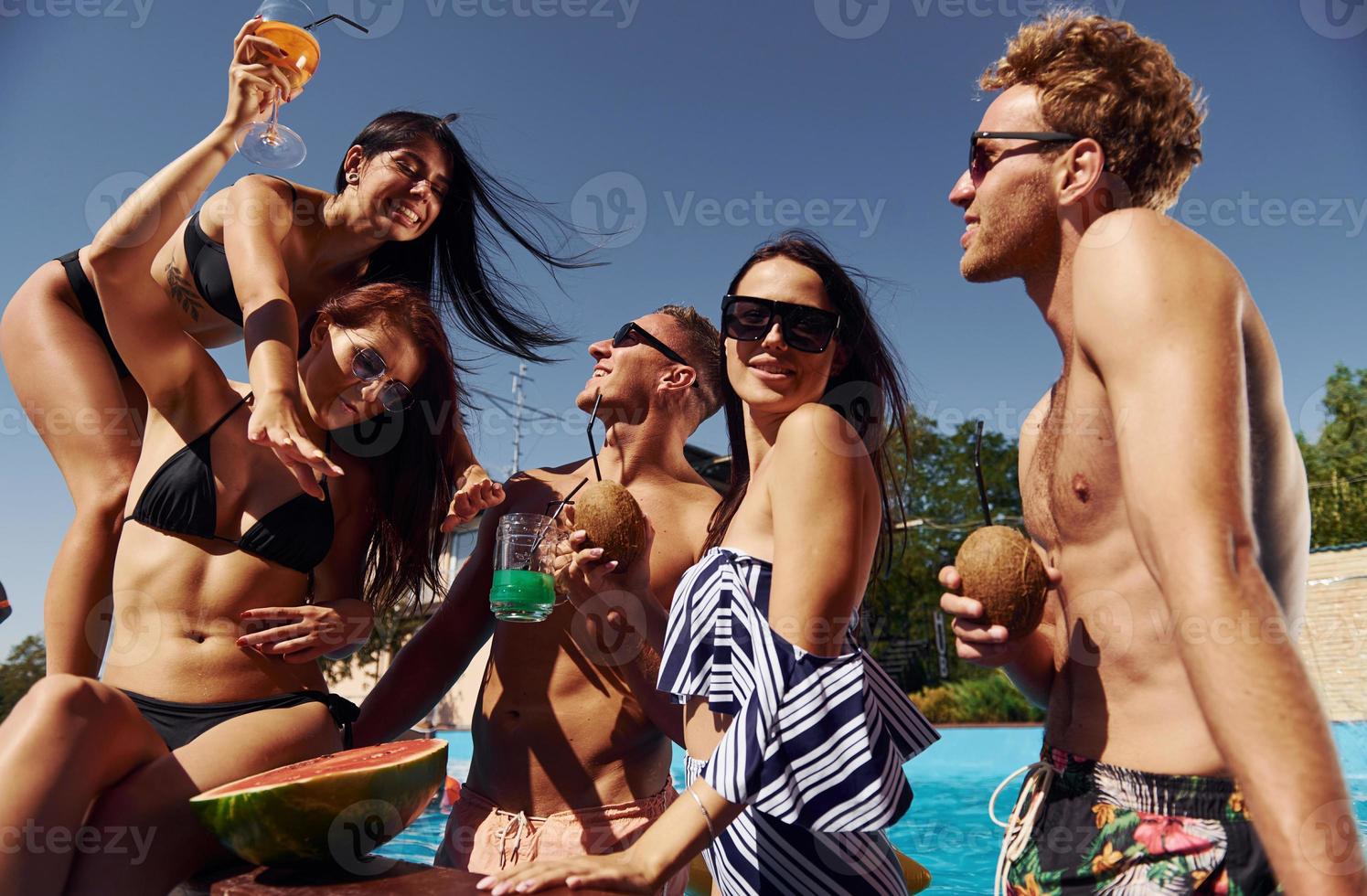 sosteniendo sandía. un grupo de jóvenes felices se divierten en la piscina durante el día foto
