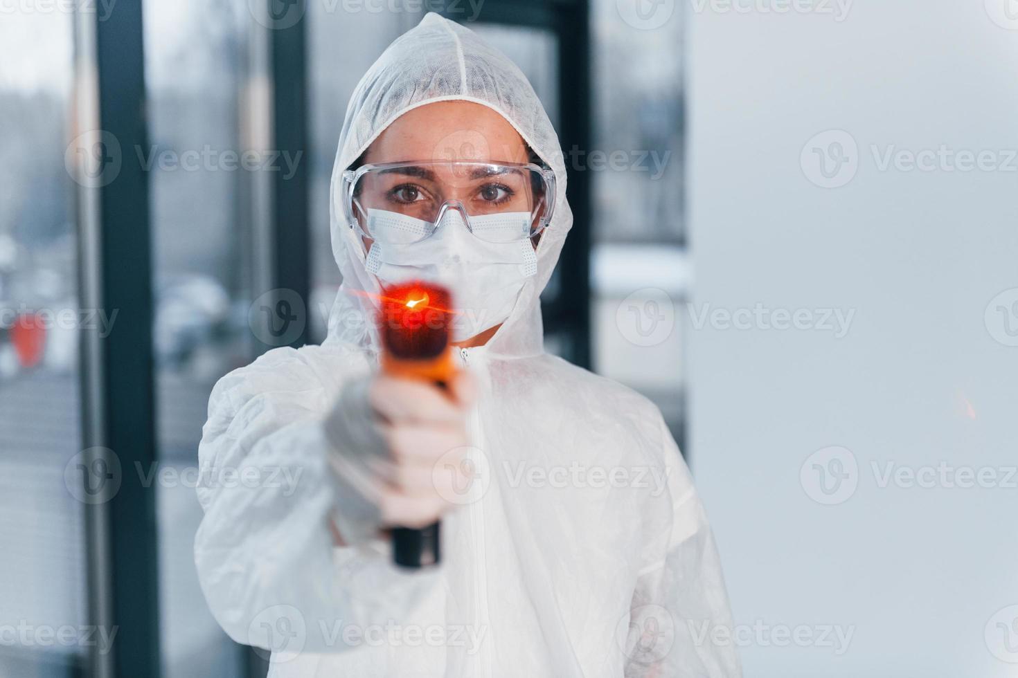 sostiene termómetro infrarrojo. retrato de una doctora científica con bata de laboratorio, anteojos defensivos y máscara foto