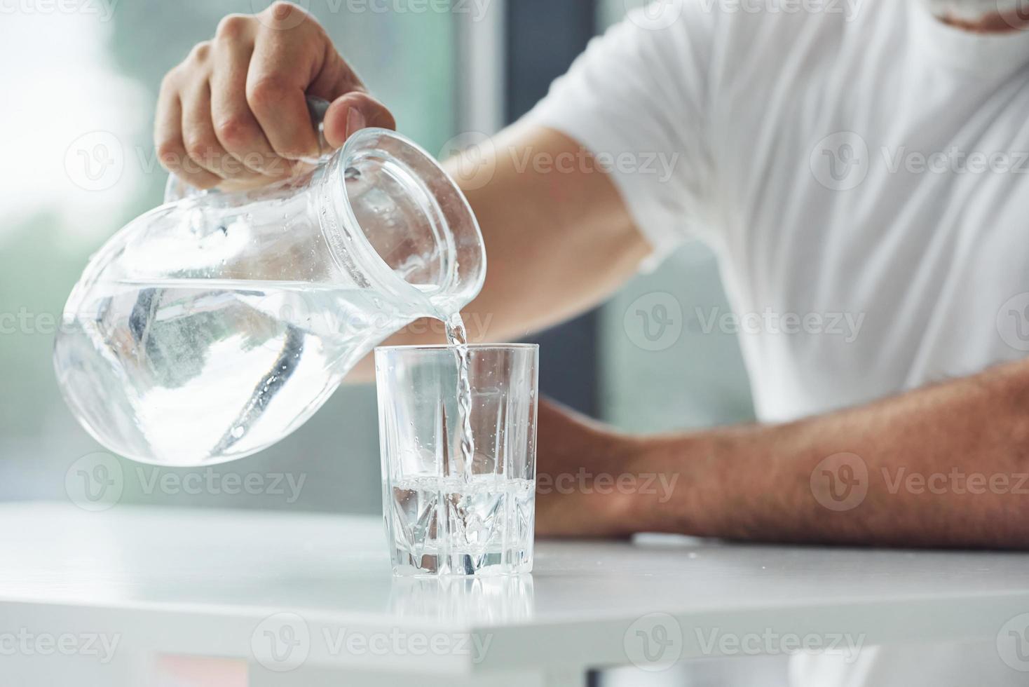 Close up view of man that sits by table and pouring water into glass photo