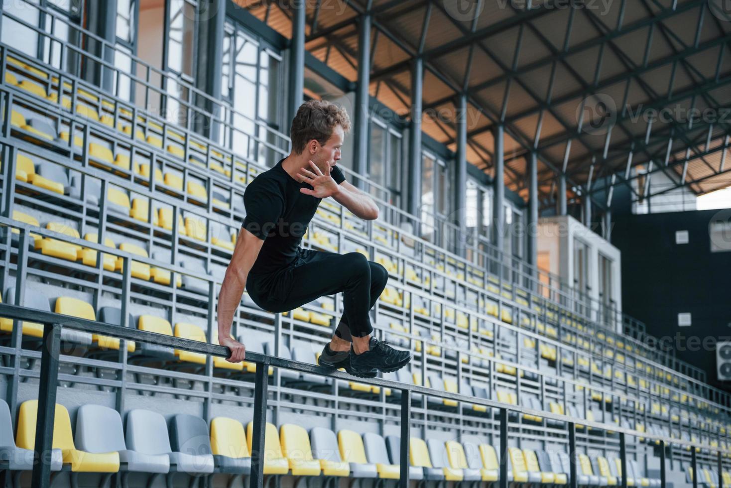 saltando y haciendo parkour en las gradas. chico joven deportivo en camisa negra y pantalones al aire libre durante el día foto
