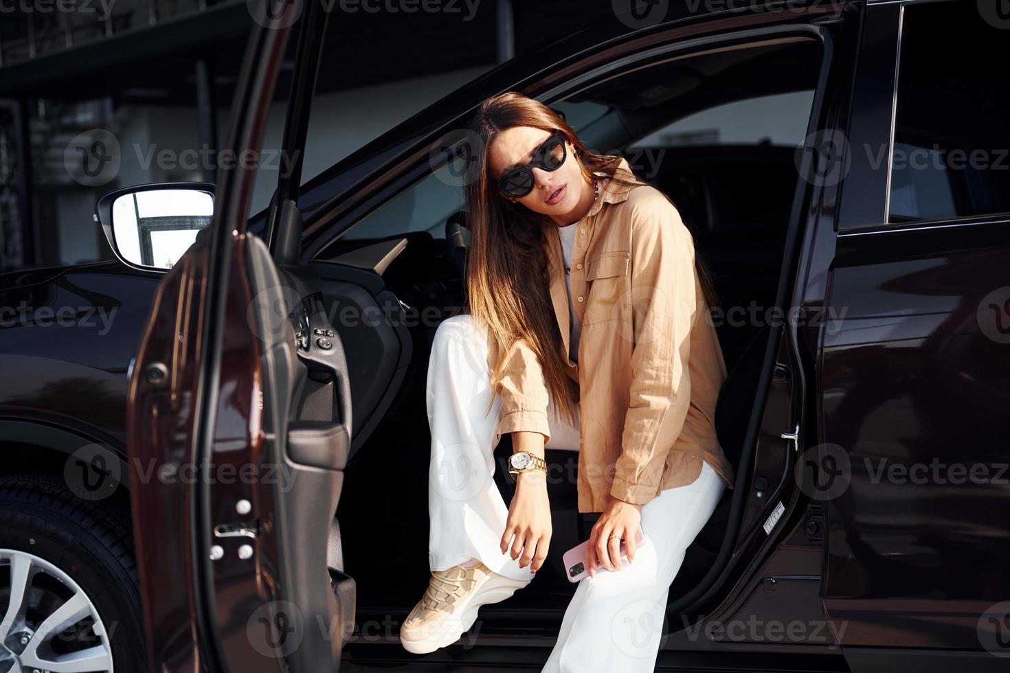 Sits with car's window opened. Fashionable beautiful young woman and her modern automobile photo