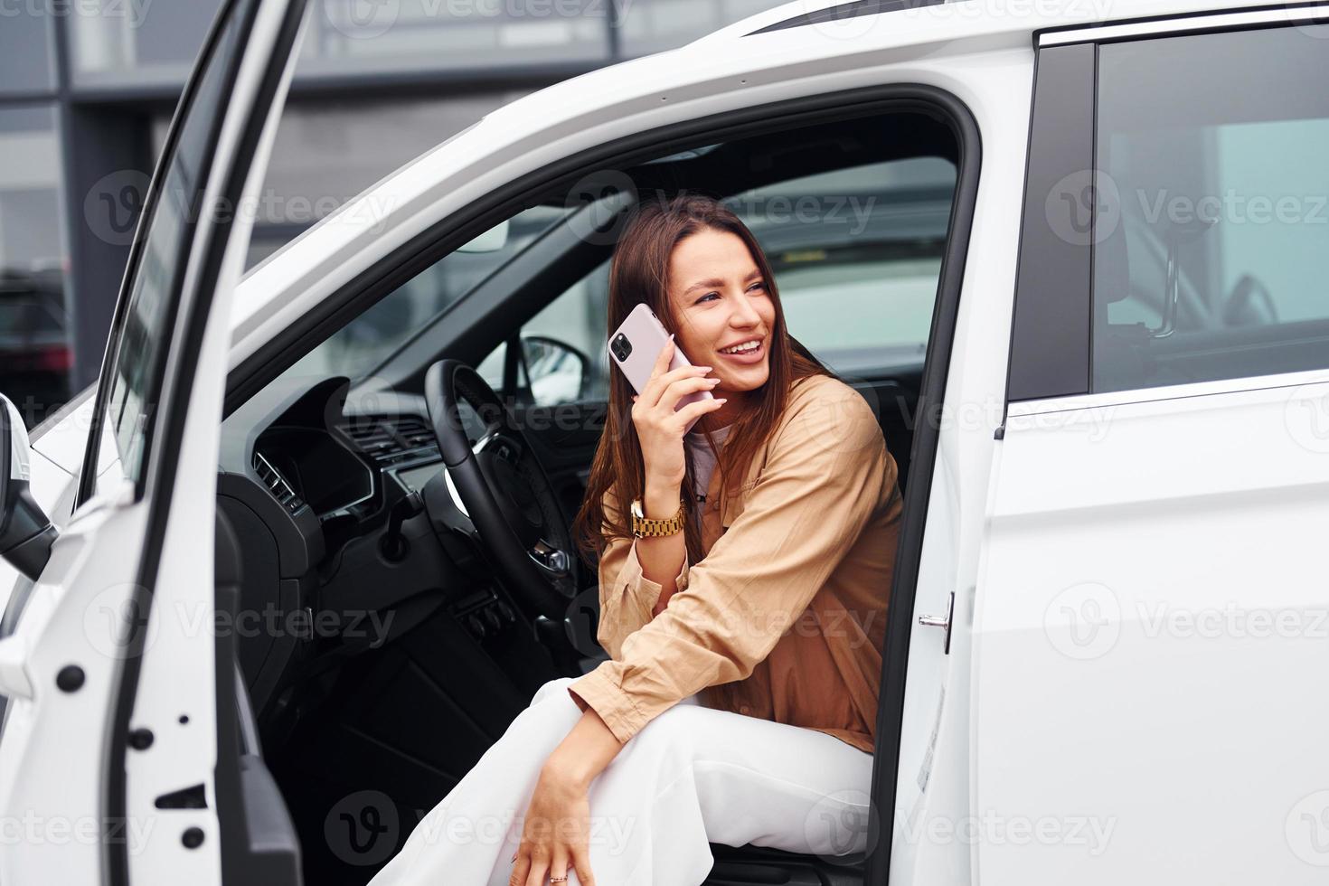 Talks by phone with door opened. Fashionable beautiful young woman and her modern automobile photo