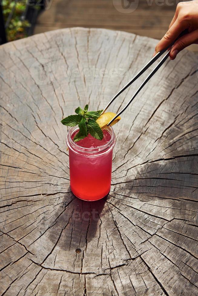 mano del camarero. con limón y menta. vista de cerca del cóctel alcohólico de verano fresco en la mesa de madera foto