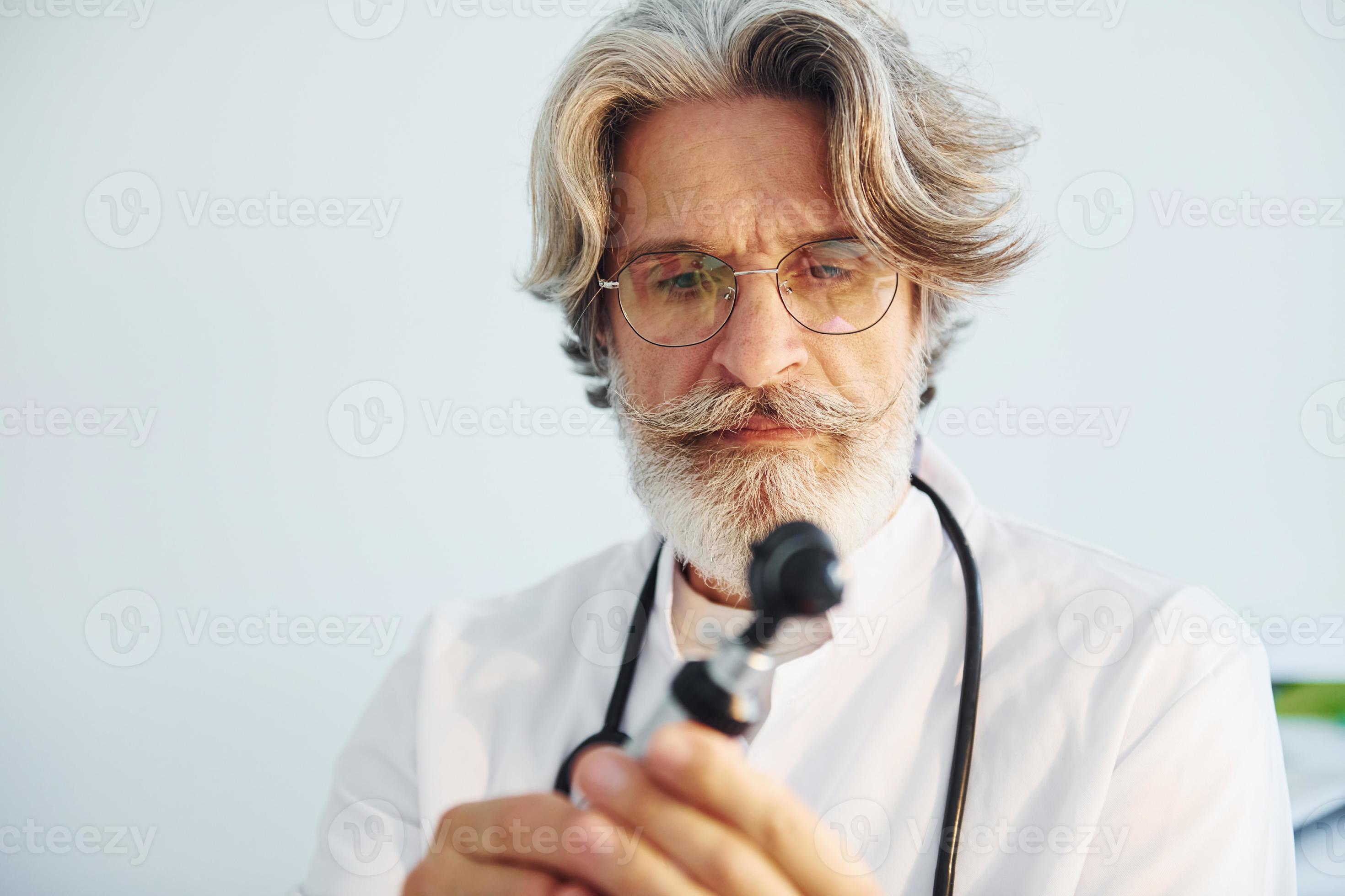 Portrait of senior male doctor with grey hair and beard in white coat