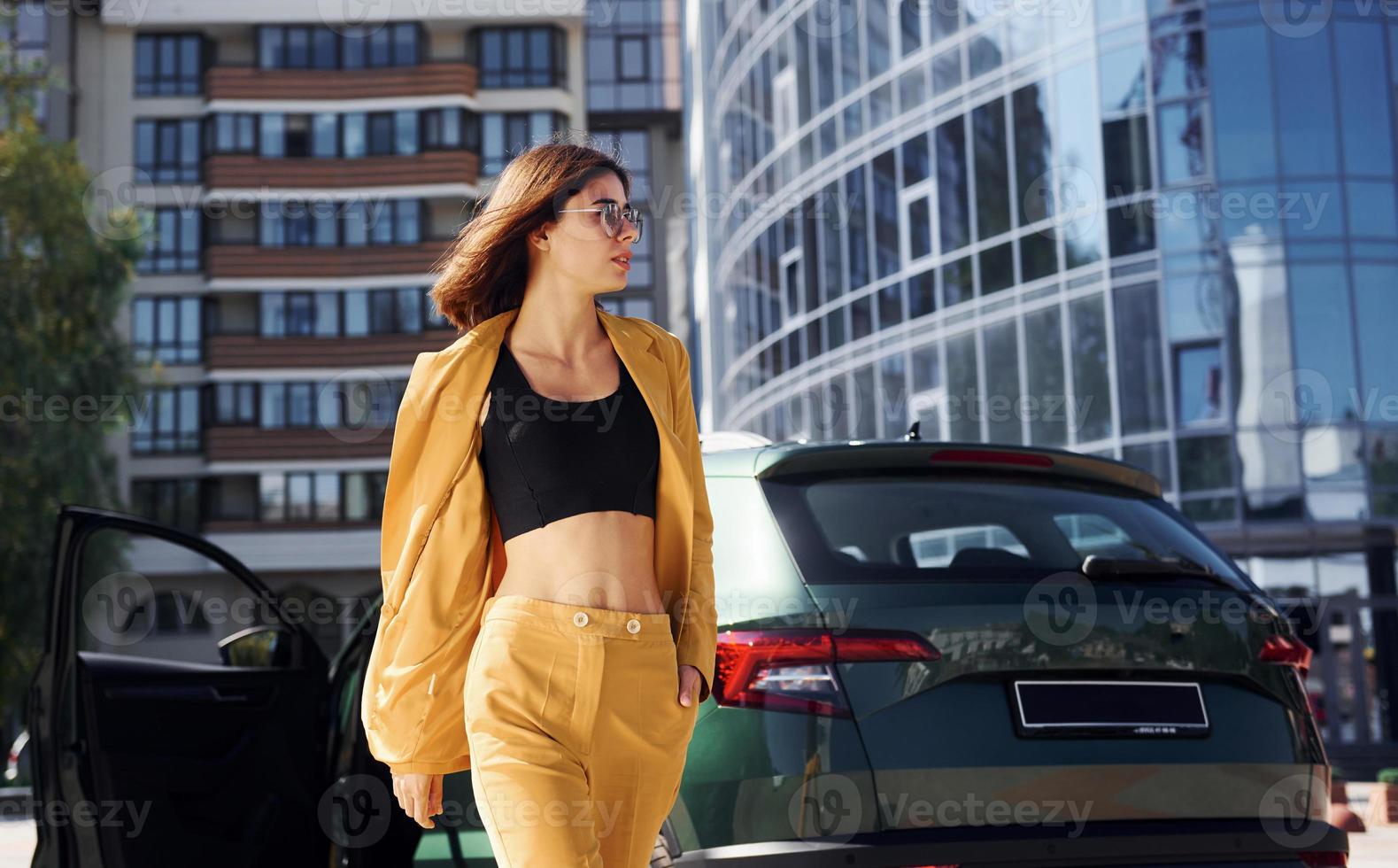 camina hacia adelante desde el automóvil. joven mujer de moda con abrigo de color burdeos durante el día con su coche foto