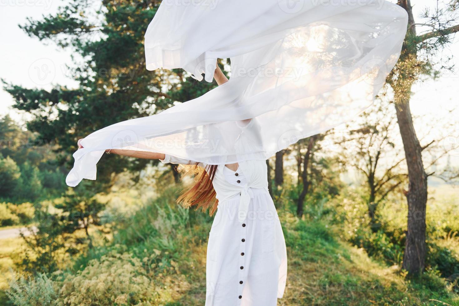 Happy young woman dancing with white cloth in hands outdoors in the forest photo