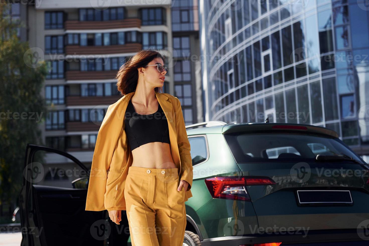 Walks forward from automobile. Young fashionable woman in burgundy colored coat at daytime with her car photo