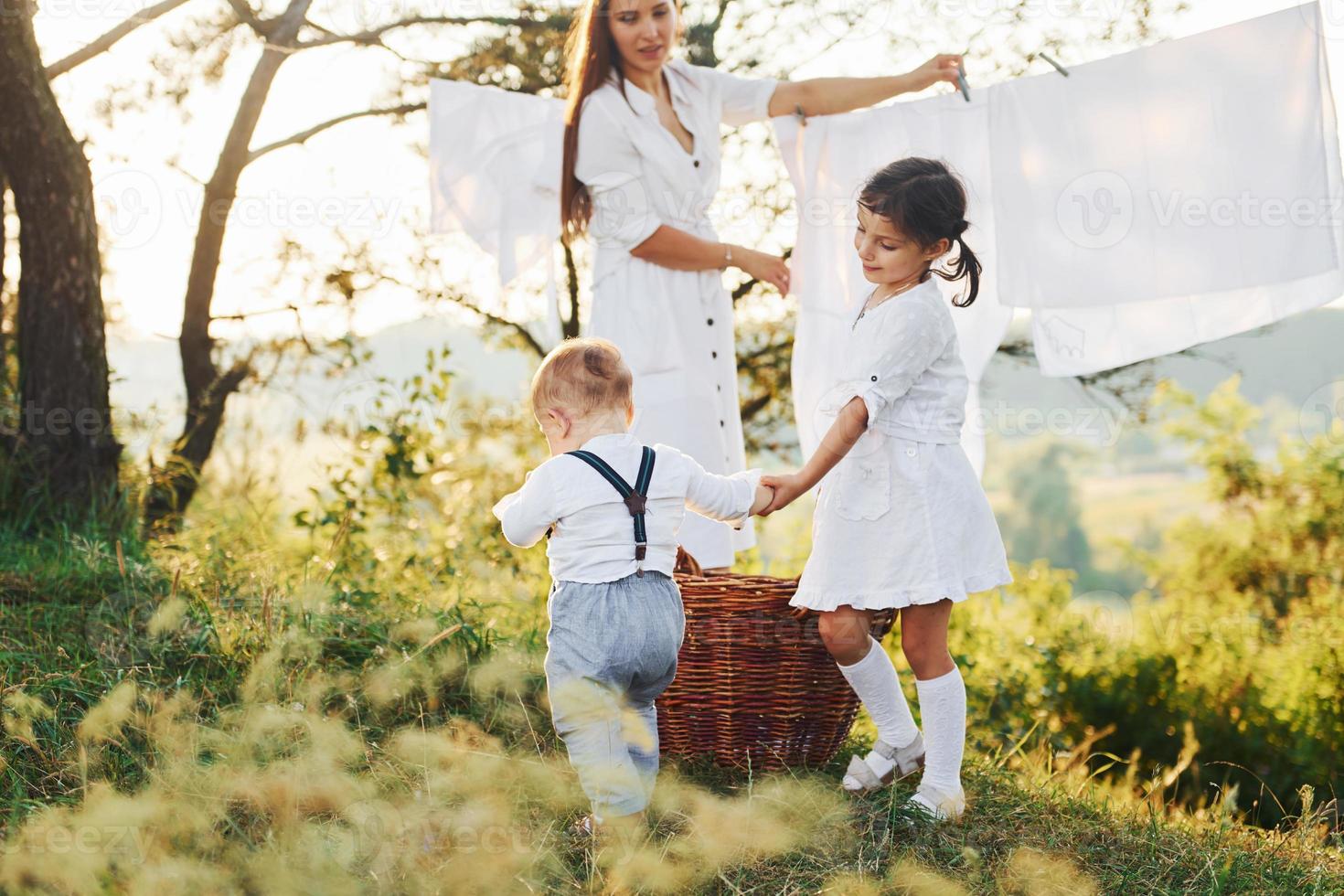 Housewife drying clothes. Young mother with her little daughter and son is outdoors in the forest. Beautiful sunshine photo