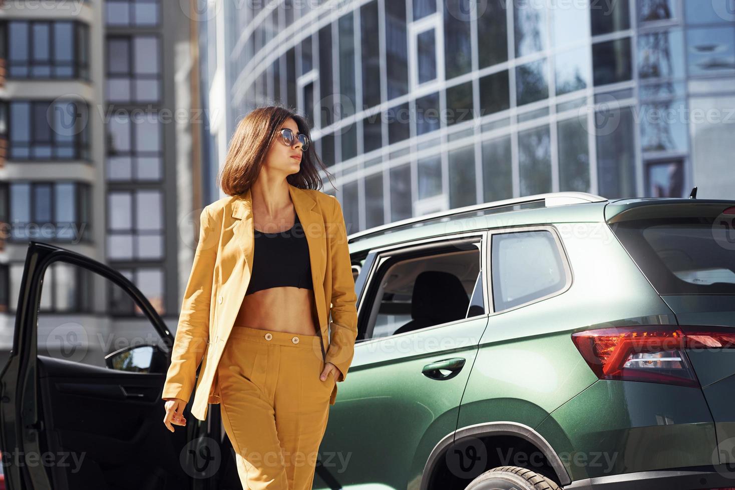 Young fashionable woman in burgundy colored coat at daytime with her car photo
