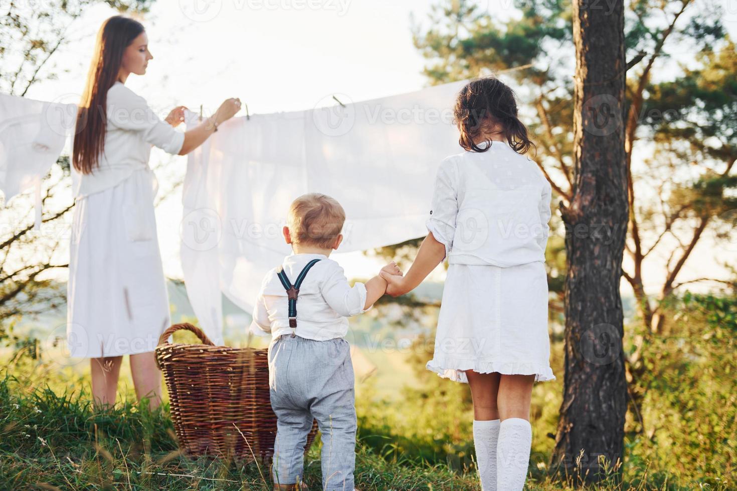 Housewife drying clothes. Young mother with her little daughter and son is outdoors in the forest. Beautiful sunshine photo