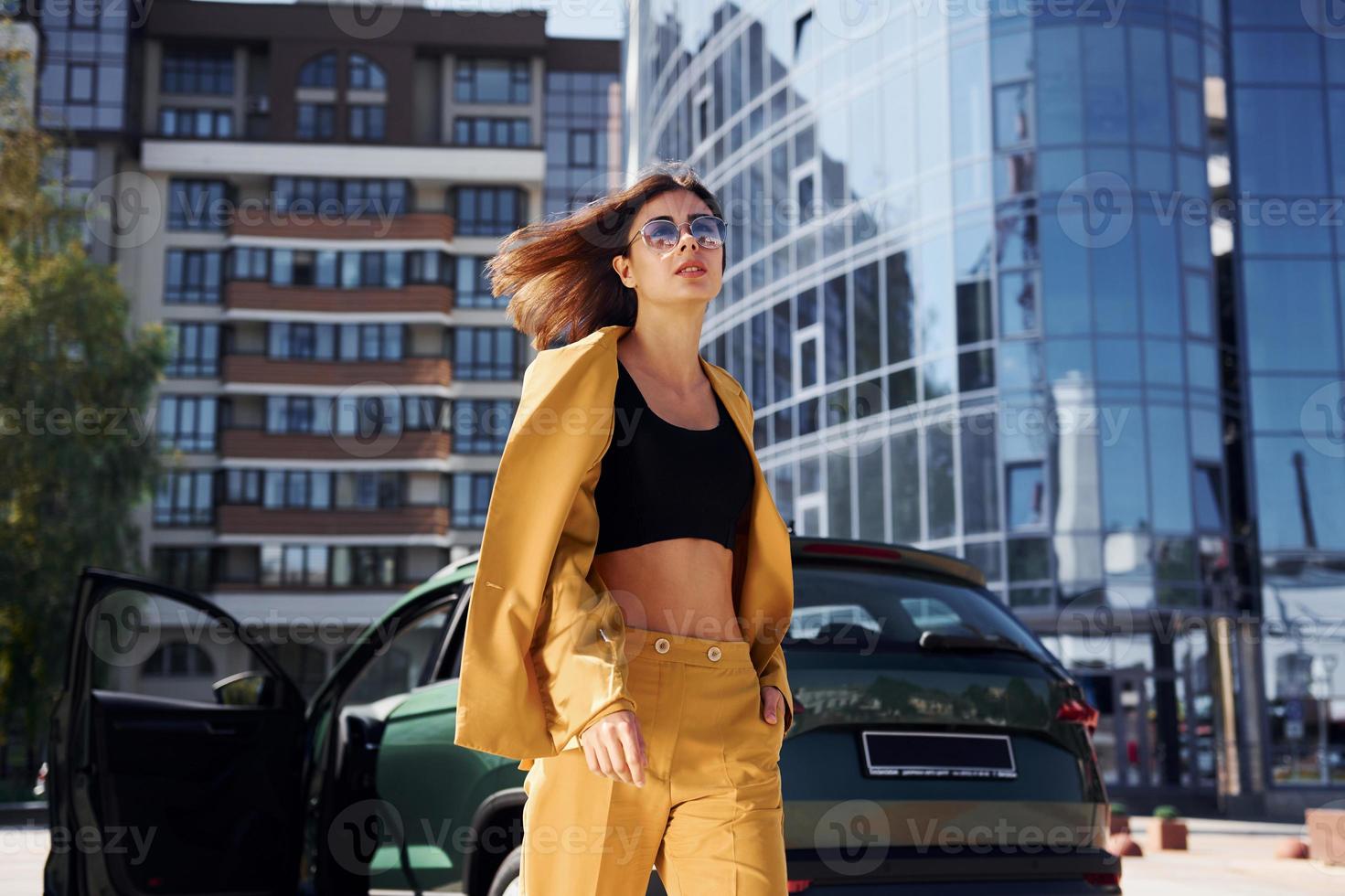 Walks forward from automobile. Young fashionable woman in burgundy colored coat at daytime with her car photo