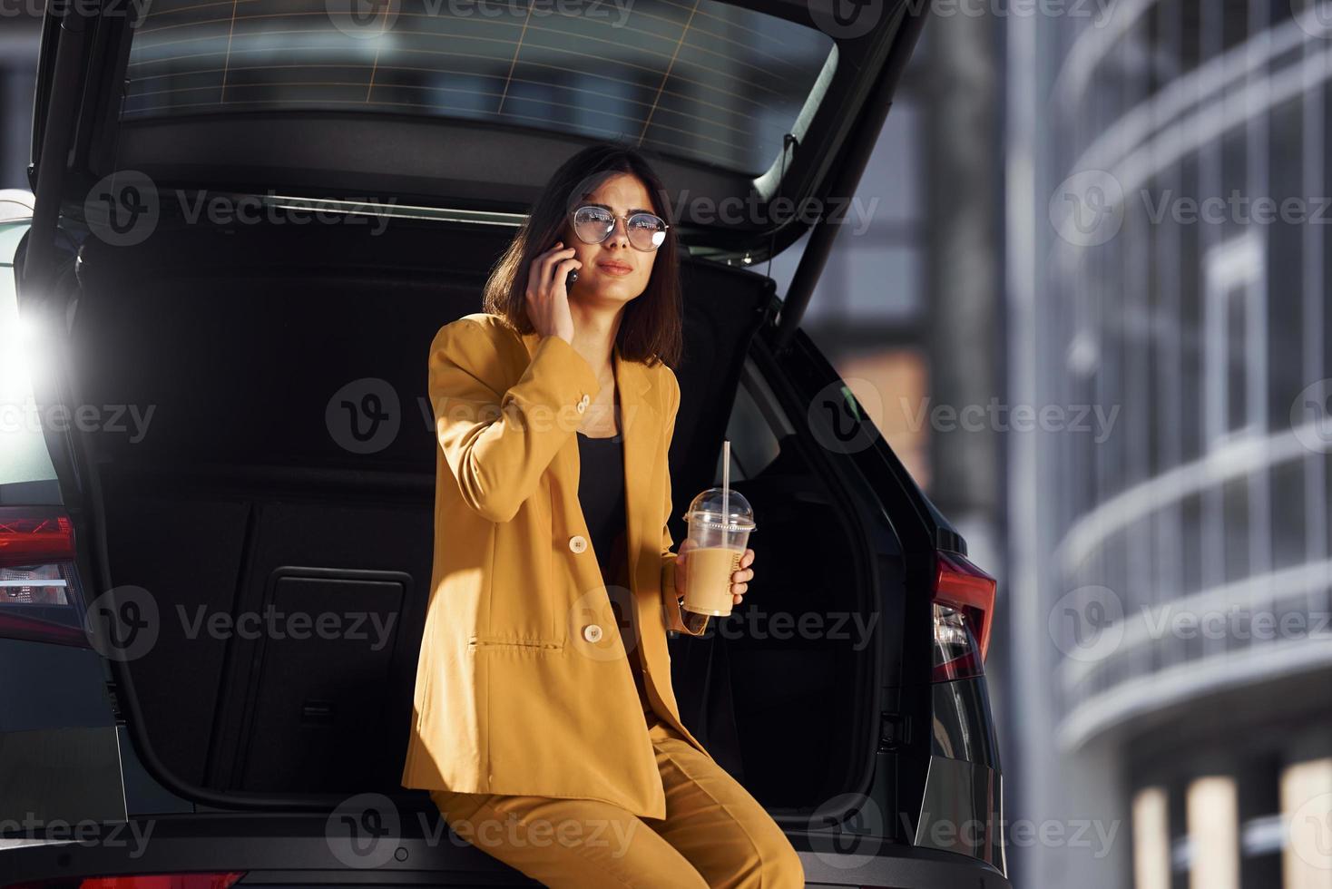 Talks by phone. Young fashionable woman in burgundy colored coat at daytime with her car photo