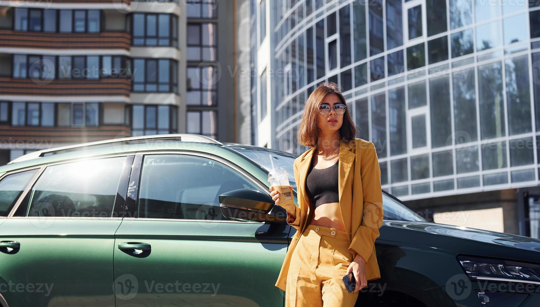 Young fashionable woman in burgundy colored coat at daytime with her car photo