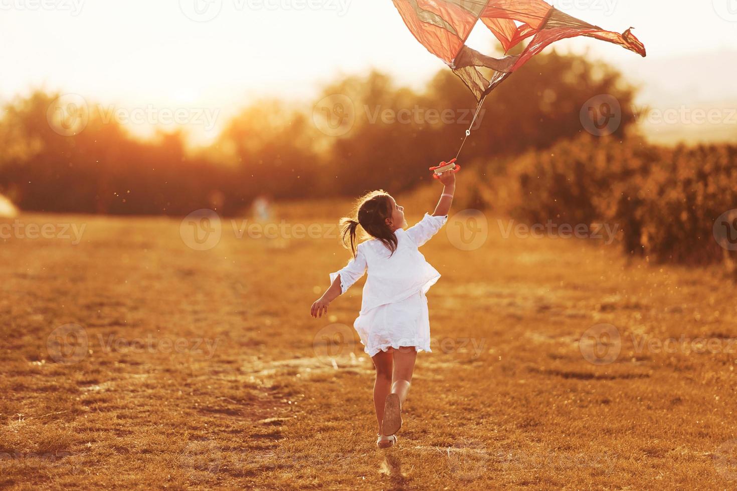 Little girl in white clothes running with kite outdoors on the field photo