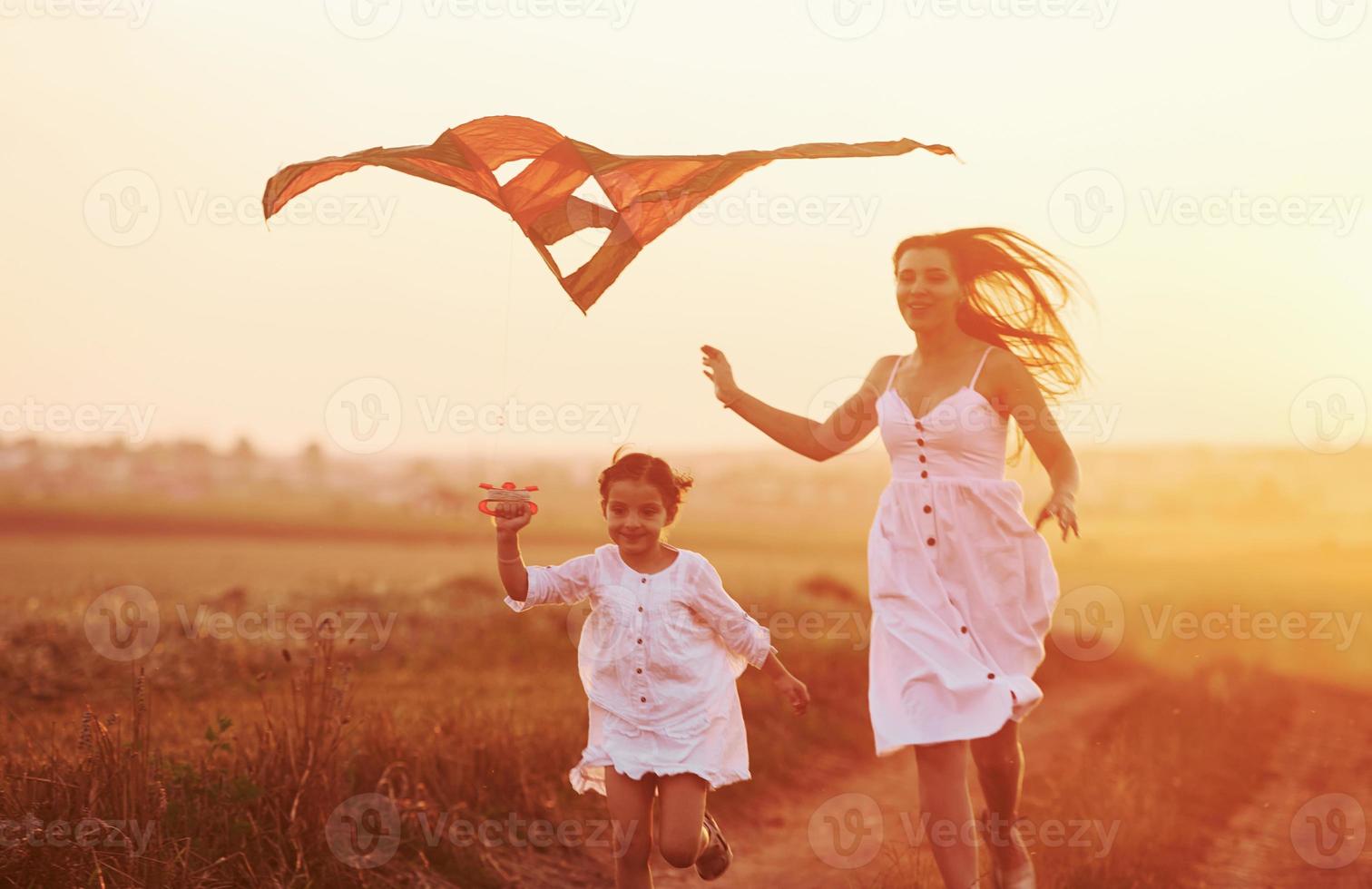 feliz madre con su pequeña hija diviértete jugando con cometas al aire libre en el campo foto