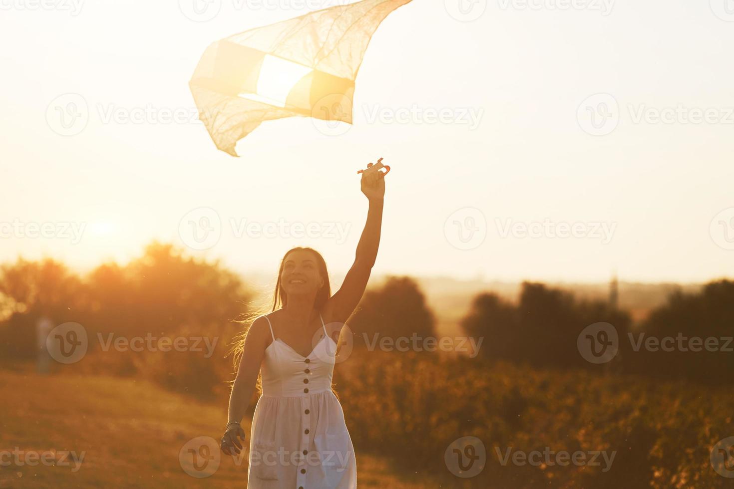 Cheerful woman having fun with kite outdoors on the field at summertime and smiles photo